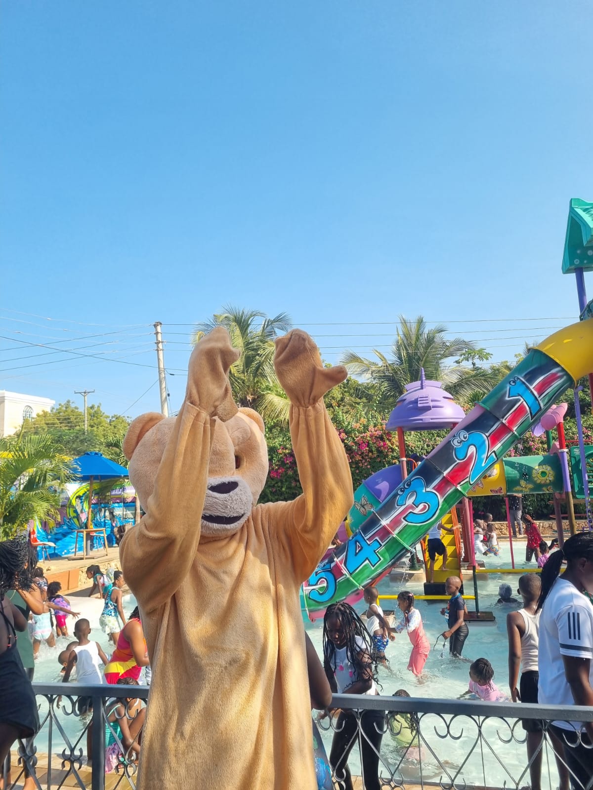 Bear mascot waving at happy kids playing in the splash zone pool